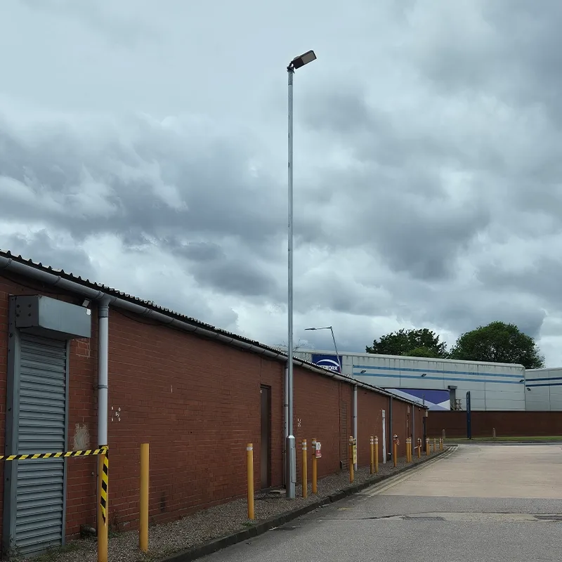 Tall galvanised area lighting column installed between commercial units